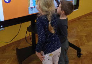 Dzieci pracują w parach przy monitorze interaktywnym.